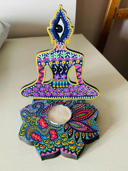 This Buddha candle holder features a third eye design and is painted in cool tones of blue and purple, bringing a calming energy to your space.