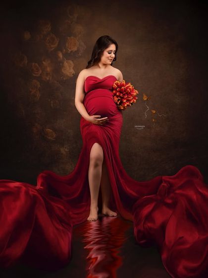 A stunning portrait featuring a vibrant red gown with a long, flowing train. The water reflection effect on the floor adds a unique and artistic dimension to this glamorous shot.