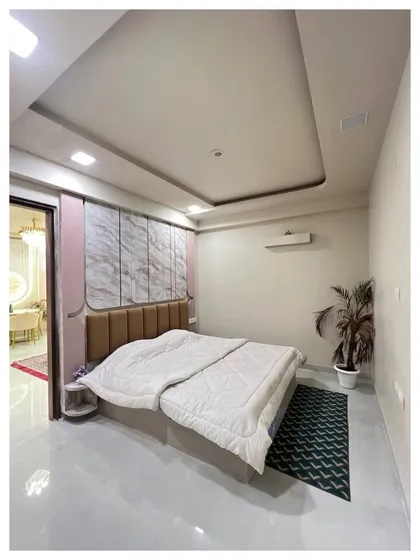 A bedroom view showing a tufted headboard against a wall with pink and marble-finish panels. The design is simple yet elegant, focusing on a mix of textures and soft colors.