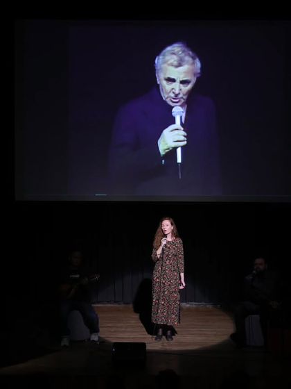 A singer performs on stage, with a large projection of Charles Aznavour behind her. We use multimedia elements to create a rich, immersive experience during our tribute concerts.
