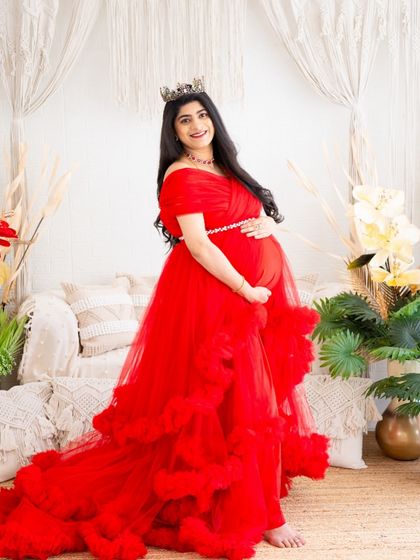A full view of one of our most popular red gowns. This shot captures the rich color and texture of the dress in our fully styled studio, making the mom-to-be the center of a beautiful scene.