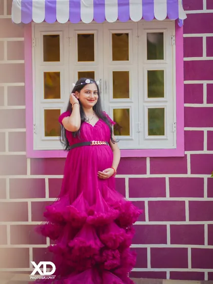 A beautiful solo portrait of the mother-to-be in a magenta gown against a colorful brick wall.