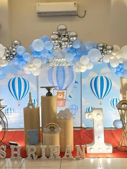 A charming hot air balloon themed first birthday party. The blue and white color scheme, cloud-like balloons, and hot air balloon props create a dreamy 'up, up and away' feeling.