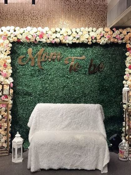 Another view of the elegant 'Mom To Be' foliage wall decoration. The soft lighting highlights the texture of the green wall and the delicate pastel floral frame.