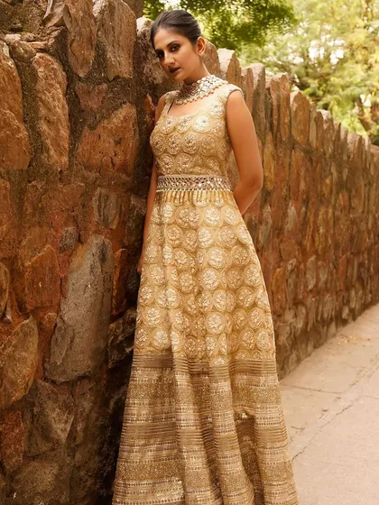 A closer view of the model against the stone wall, focusing on her confident gaze and the detailed choker necklace that complements the golden gown. This shot balances the outfit with the model's personality.