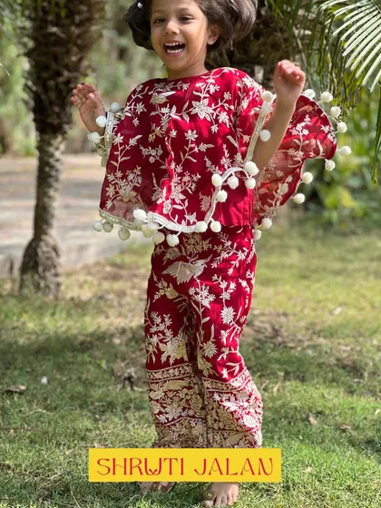 A joyful shot of a little girl in my maroon floral cape set, jumping with happiness. My clothes are made for movement and play.