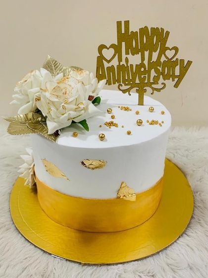 A classic white and gold anniversary cake. The simple elegance of the golden band and white floral topper makes it a timeless choice.