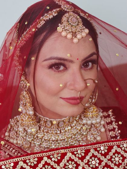 A peek-a-boo shot through the dupatta, focusing on the bride's expressive eyes and the heavy pearl and kundan jewellery.