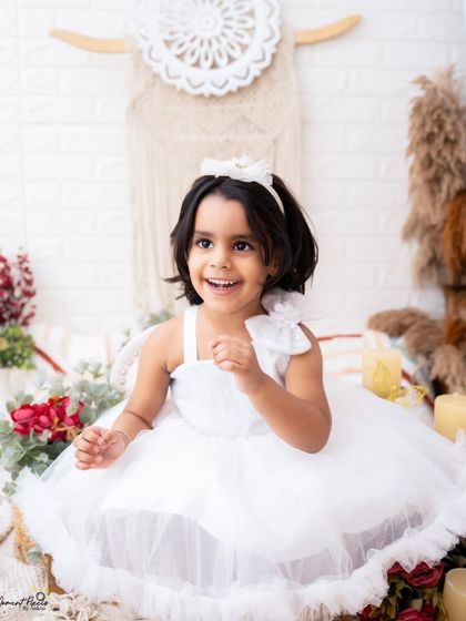 A radiant smile from a pretty little girl in white. Her happiness is infectious in this bright and airy studio portrait.