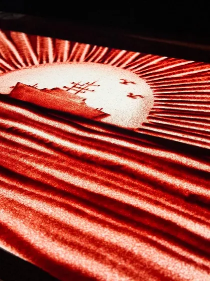 A sunrise over the ocean with a naval ship, etched in sand. This scene from the Eastern Naval Command tribute represents hope, vigilance, and the dawning of a new era for the fleet.