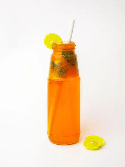 A bright orange iced tea or cooler in a glass bottle, garnished with a lemon slice.