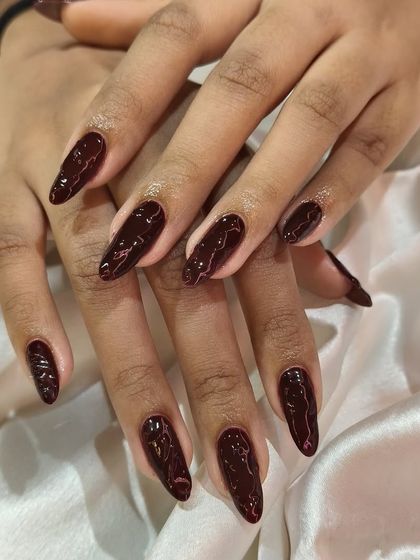 A deep maroon gel polish with a subtle, elegant swirl pattern. This design adds a touch of texture and sophistication to a classic dark manicure on almond-shaped nails.