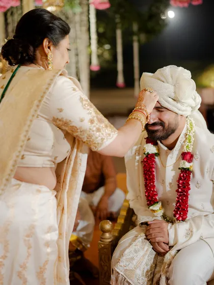 The mother of the groom applying a tilak to her son. Her classic ivory and gold saree is a perfect example of timeless elegance that never goes out of style.