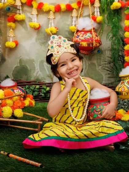 A joyful portrait of a little Radha with a big smile, surrounded by the vibrant colors of the Janmashtami theme.