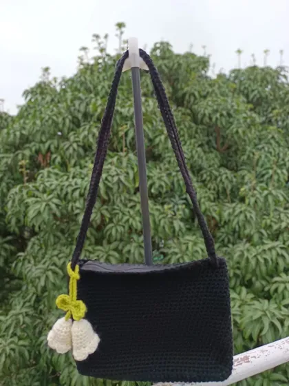 A custom black shoulder bag with a white tulip charm. The contrast of the black bag with the light charm makes for a striking design.