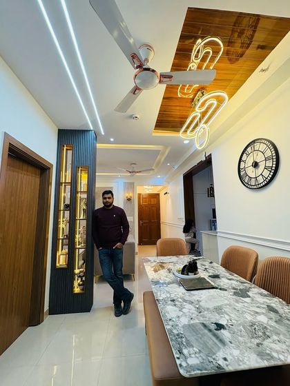 A view of the dining area in a completed project, with a marble-top table, comfortable chairs, and a unique neon light feature on the wooden ceiling panel.