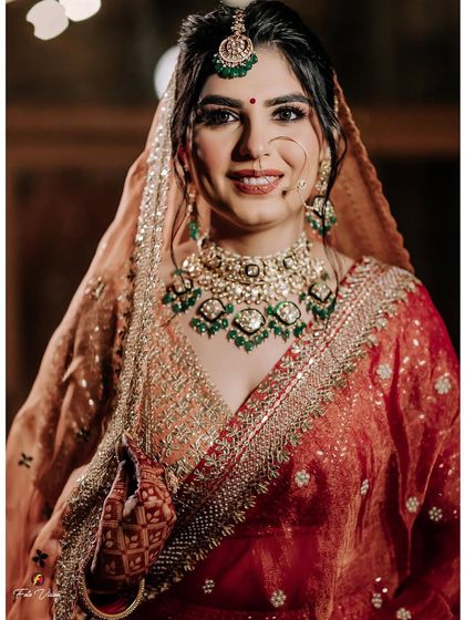A smiling close-up of the bride, showcasing her beautiful green and gold jewelry and the red bindi, a classic bridal detail.