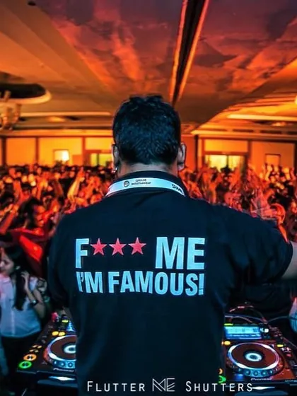 From the back, facing a massive crowd in a grand ballroom. The "F*** Me I'm Famous!" shirt is a nod to the classic party vibe, all in good fun.