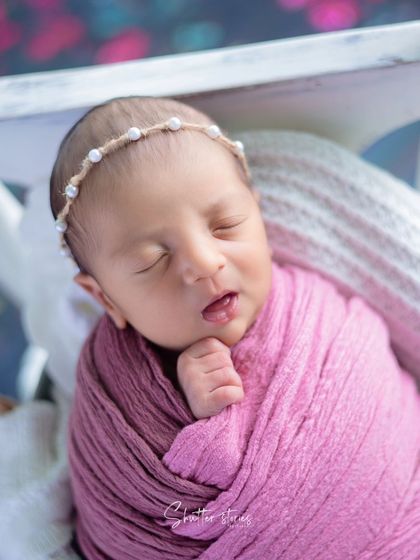 A newborn wrapped in pink rests in a white hanging prop against a beautiful bougainvillea backdrop.