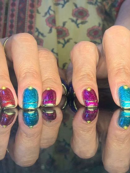 A vibrant and colorful set of short nails with multi-colored glitter and metallic finishes.