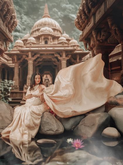 A dramatic, wide-angle shot of a mom-to-be at a temple-inspired water set. The flowing fabric of her saree adds a sense of grandeur to the scene.