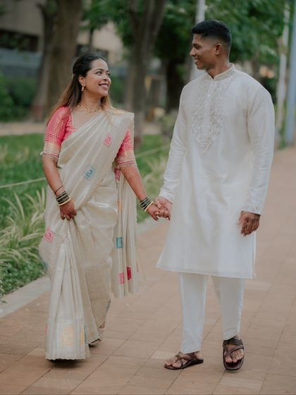 A full-length shot of a couple walking hand-in-hand during their engagement photoshoot. The bride's elegant saree and the groom's classic kurta create a timeless, graceful image.