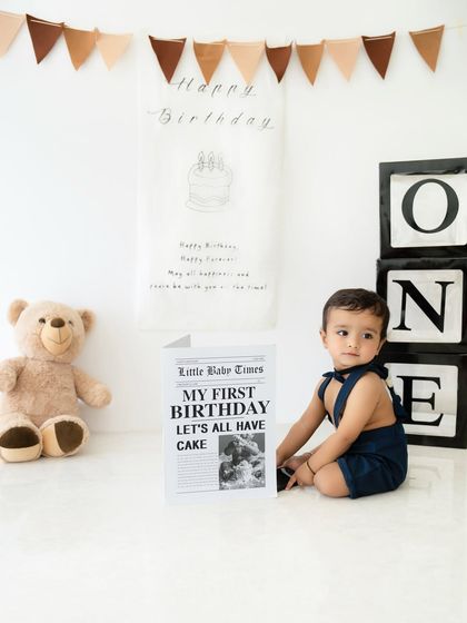 A sweet moment from a first birthday shoot, where the baby sits beside a custom "Little Babe Times" newspaper prop announcing his big day.