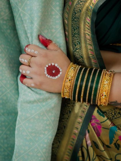 A close-up on the bride's hand, adorned with traditional Bengali 'Aalta' and green bangles, resting gently on her partner's arm. A beautiful detail shot of cultural traditions.