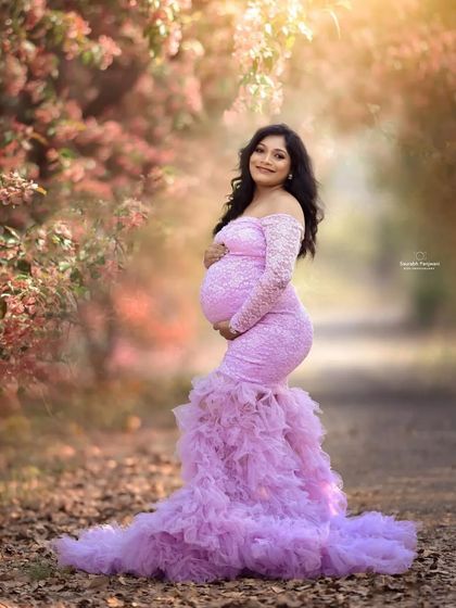 A fairytale moment in a sun-drenched lane. This lavender mermaid-style maternity gown features delicate lace sleeves and a dramatic ruffled train. It hugs the body to beautifully showcase your baby bump.