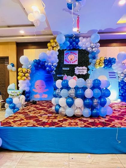 A wide view of a Boss Baby themed party on a stage. The setup includes multiple character cutouts, a custom backdrop, and extensive blue, white, and silver balloon decorations.