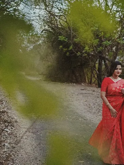 A wide shot of a woman in a red saree on a country road, with a dreamy, slightly blurred effect adding to the artistic mood.