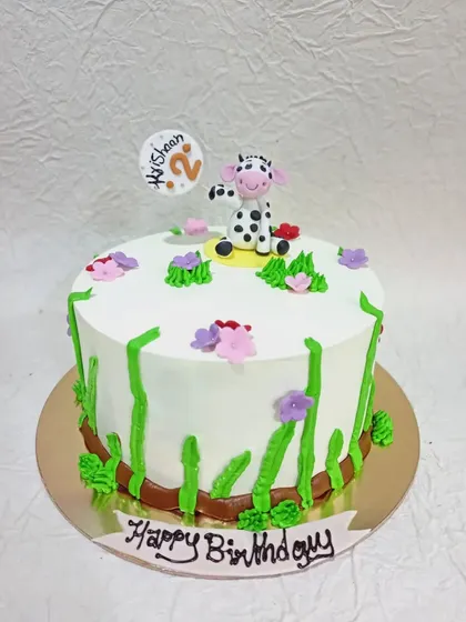 A simple and sweet cake with a cute cow topper. The green piped grass and little flowers give it a lovely farm-fresh feel.