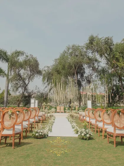 The view down the aisle, lined with elegant chairs and white floral arrangements, leading to a stunning mandap area under the trees. This is outdoor elegance at its finest.