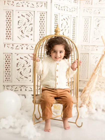 Capturing the playful spirit of toddlers is one of my joys. This portrait uses a boho-themed setup with a golden birdcage chair and soft textures to create a whimsical atmosphere.