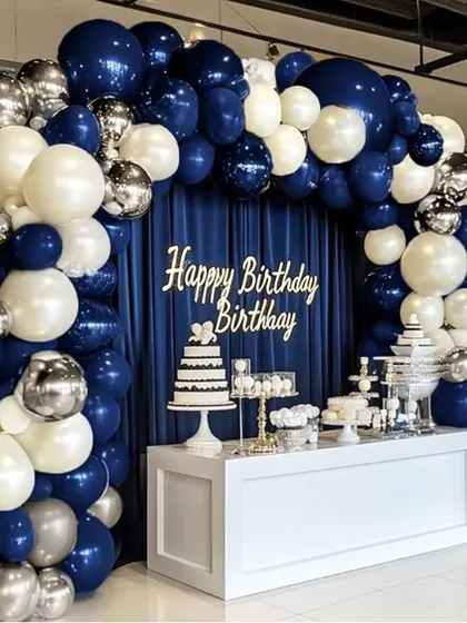 This elegant cake table setup shows how a classic color combination can create a big impact. The deep blue and white organic balloon arch is accented with silver chrome balloons, framing the dessert station beautifully for a stylish celebration.