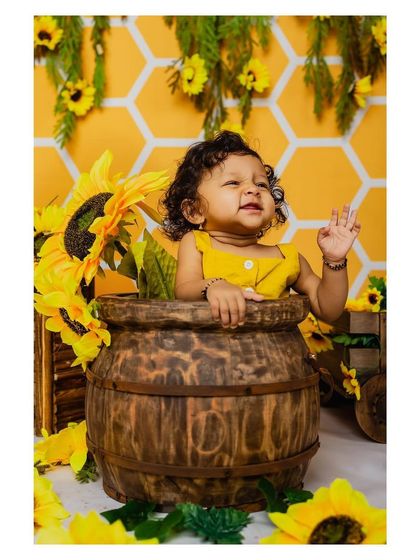 A cute baby waves from inside a barrel in our sunflower-themed studio setup. This interactive pose creates a charming and memorable portrait.