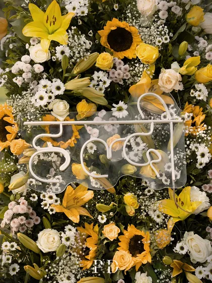 A custom neon 'Haldi' sign in Hindi, set against a backdrop of sunflowers and yellow lilies. It's a modern twist on a traditional element.