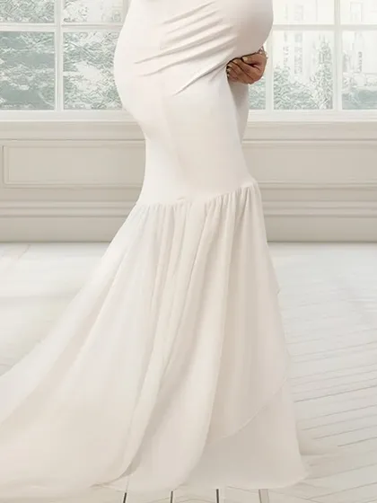 A close-up of a beautiful white mermaid-style maternity gown. The flowing train and the way it accentuates the baby bump make it a perfect choice for an elegant photoshoot.