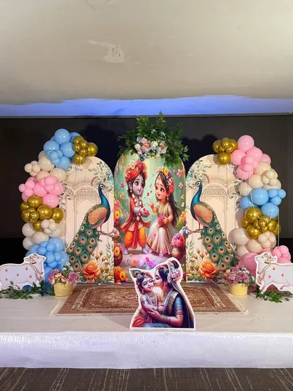 Another look at our modern Krishna-themed decor. This stage setup uses custom-printed backdrops with peacock illustrations, flanked by colorful balloon arches in pink, blue, and gold for a festive and cheerful look.