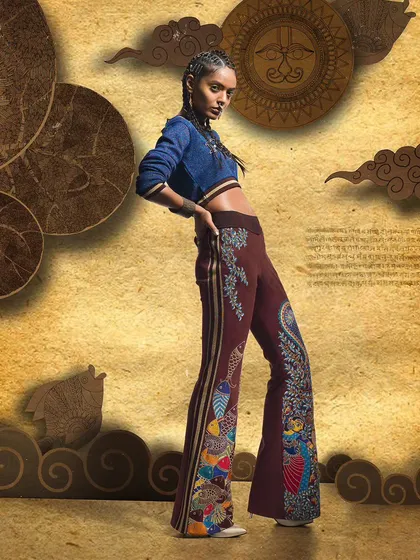 A dynamic pose highlighting flared trousers with elaborate embroidery. This shot from a designer catalogue focuses on movement and the unique silhouette of the pants against a creative, layered background.