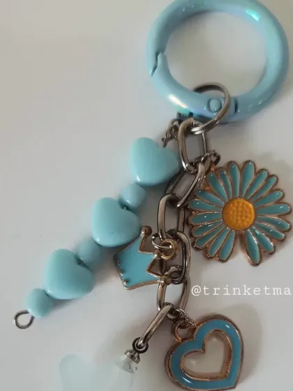 Another angle of the pastel blue charm keychain, showing the pretty combination of a daisy, crown, and heart charms.