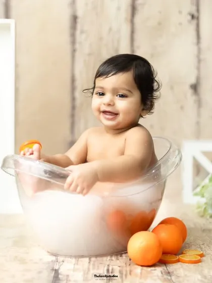A baby girl plays with an orange slice in the tub, adding a fun, interactive element to the photoshoot.