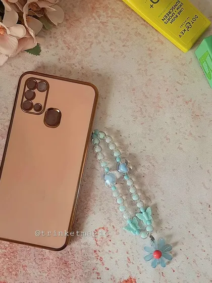 Bead your way to a stylish phone upgrade. This image shows a light blue beaded phone charm with a flower and butterfly, next to a phone.