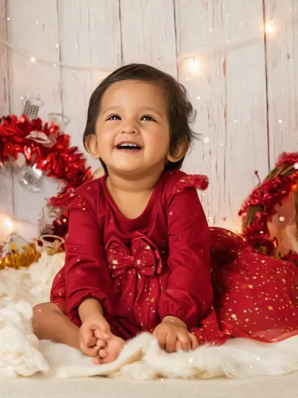 A huge, joyful smile lights up this Christmas-themed photoshoot. Dressed in a festive red dress, this little girl is surrounded by twinkling lights and holiday cheer.