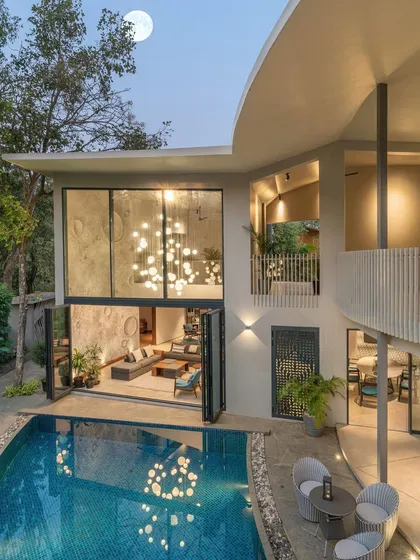 The "Moon House" features a double-height living room with a custom, crater-like textured wall, hand-plastered by local artists. The space opens completely to the pool, with the curved balcony above echoing the lunar-inspired theme.