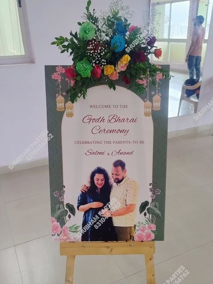 A welcome board for a Godh Bharai ceremony, featuring a photo of the parents-to-be and topped with a fresh flower arrangement.
