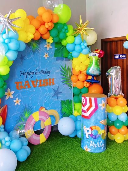 A fun and bright pool party theme. The blue backdrop is decorated with a colorful balloon garland, a lifebuoy, and other summer-themed props.