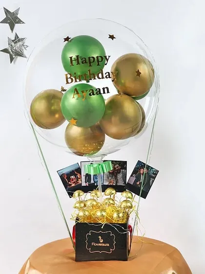 A creative hot air balloon-style bouquet. This gift includes a personalized clear balloon, a box filled with chocolates, and small photos hanging from the basket, making it a truly thoughtful present.