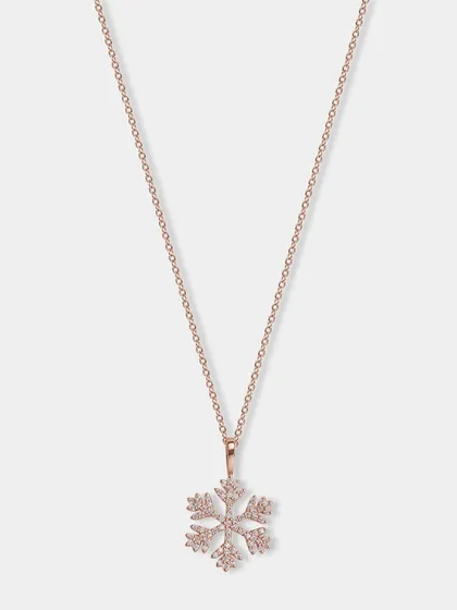 A delicate rose gold snowflake pendant necklace. The lighting is carefully controlled to make the small crystals sparkle.