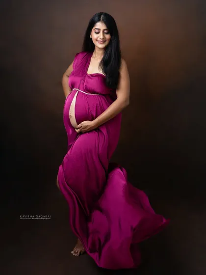 An elegant portrait of a mother-to-be, cradling her bump in a beautiful magenta gown. Her serene expression captures the quiet joy and anticipation of this special time.